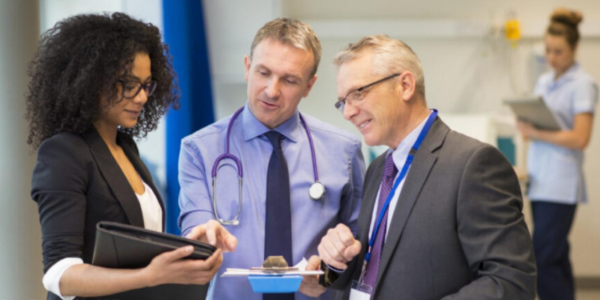 Three people stood in a hospital looking at a chart with a nurse in the background.