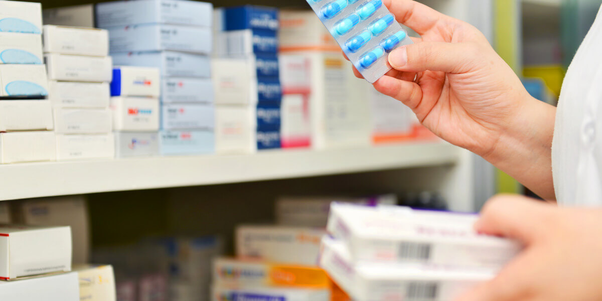Person holding a tray of blue tablets in front of shelves filled with boxes of tablets.