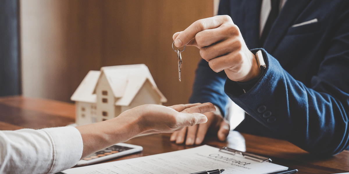 Man giving a key to someone, with a contract and a house on the table.
