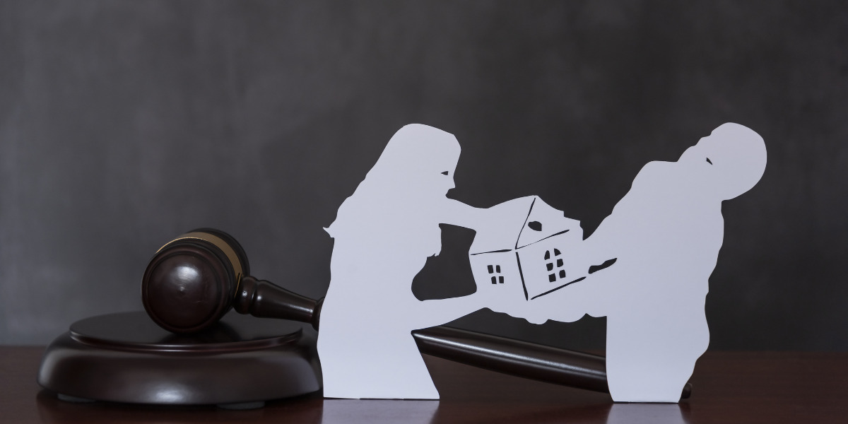 Paper cut outs of a couple fighting over a house with a gavel in the background.
