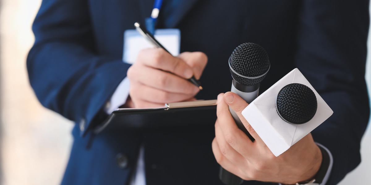 Man in a suit with a microphone and writing on a clipboard.