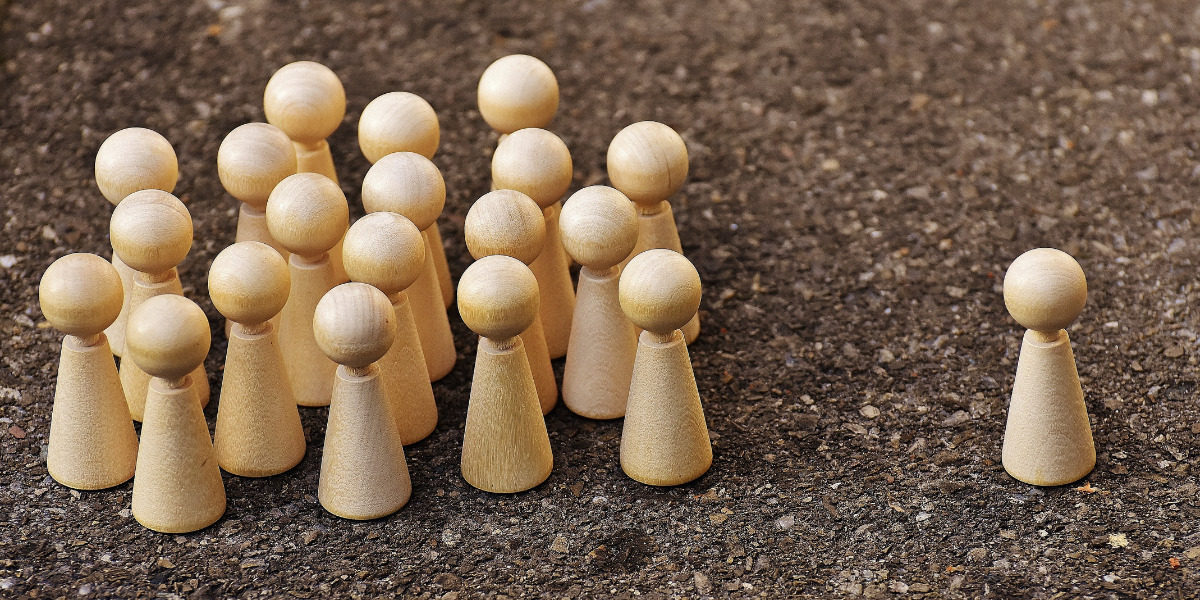 A group of wooden pawns arranged to represent a crowd, with one pawn standing apart from the rest, possibly depicting individuality or exclusion.
