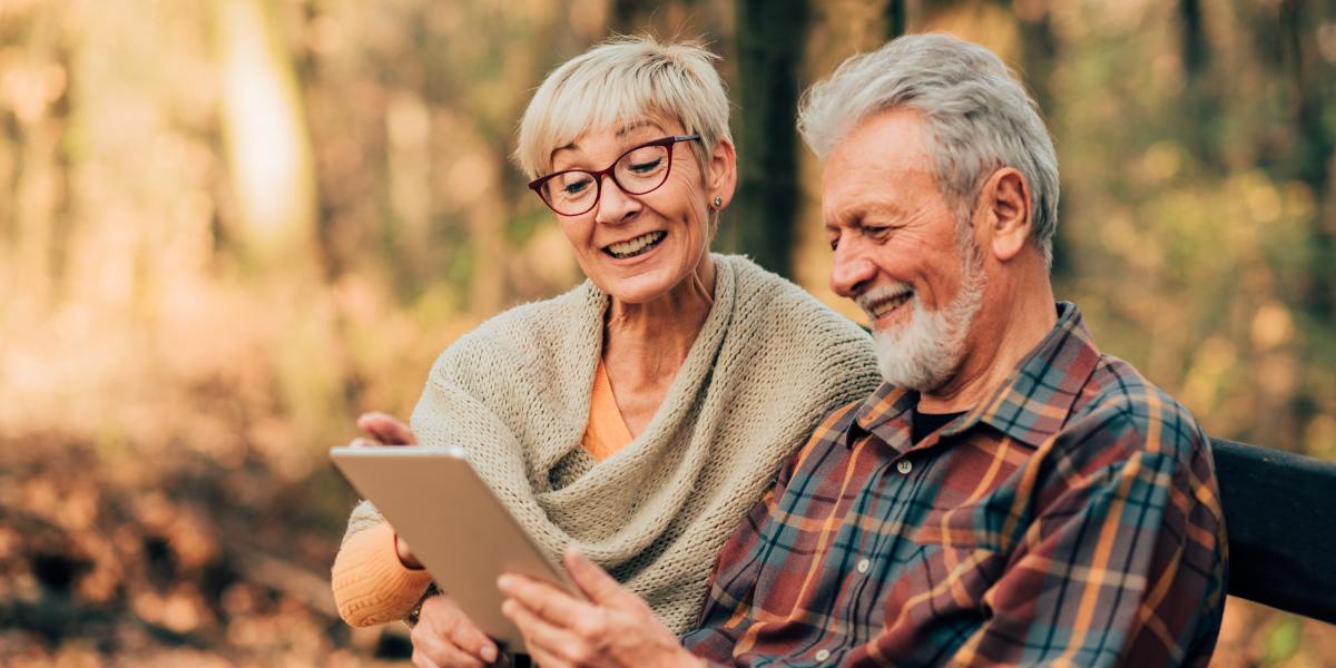 Joyful senior married couple using a digital tablet at the park