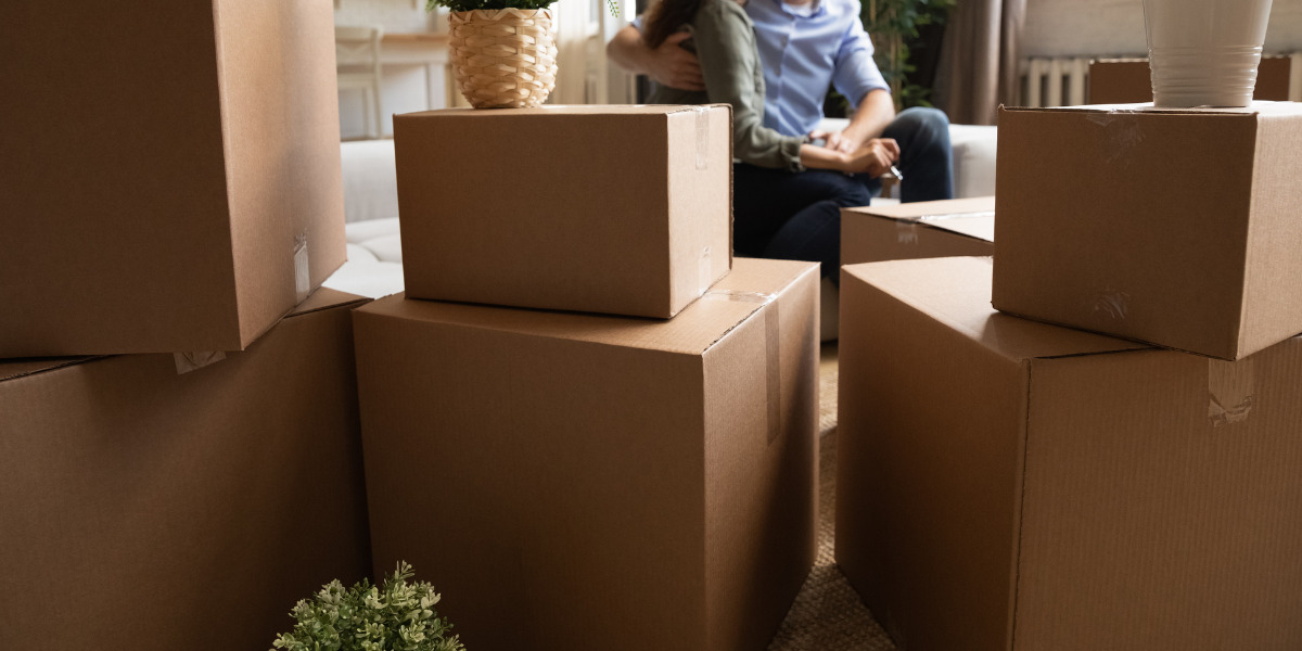 A couple takes a break surrounded by cardboard moving boxes, signaling a day of packing or unpacking in their home.