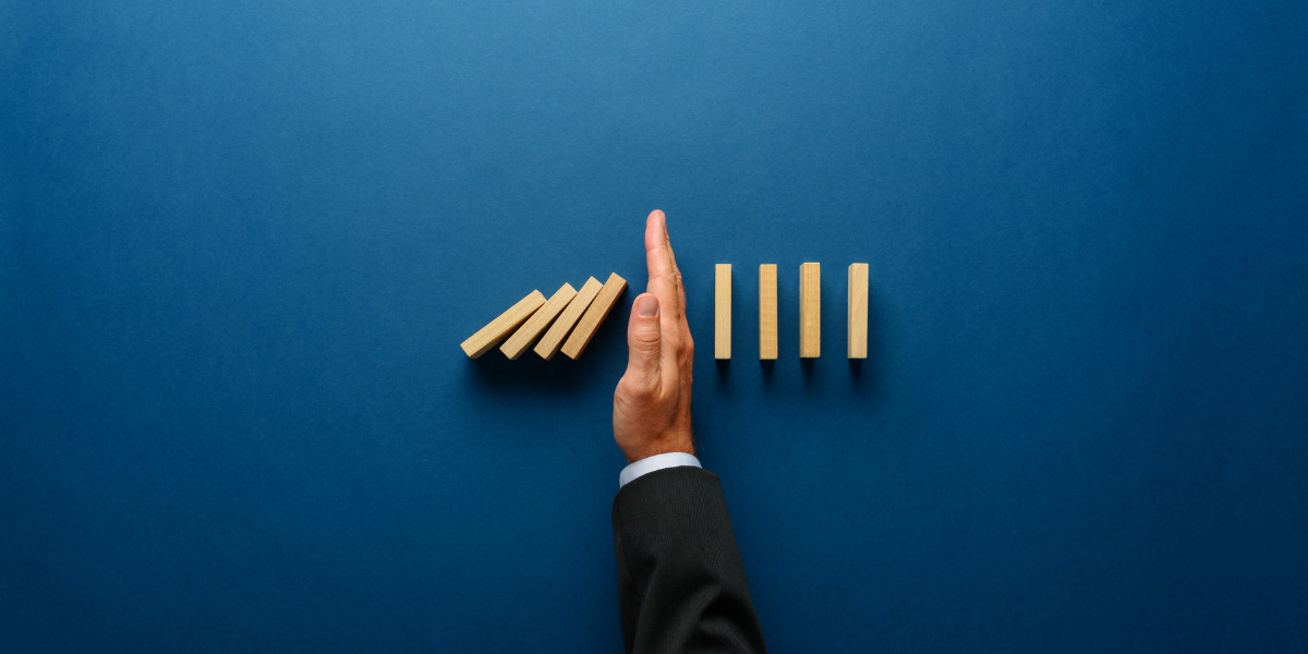 Intervention: a hand strategically stopping the domino effect on a striking blue background.
