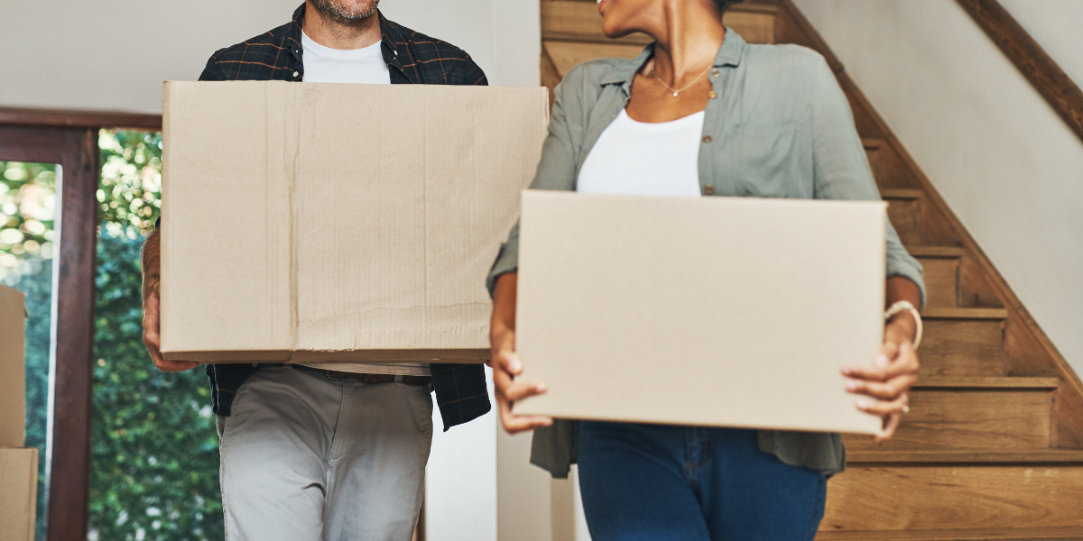 A couple carrying cardboard boxes while moving into a new home.