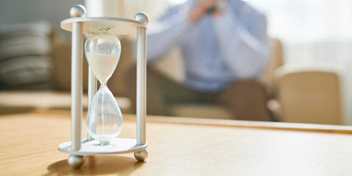 Reflecting on time, a contemplative individual is in the background, and an hourglass is in the foreground, symbolising the fleeting nature of time.