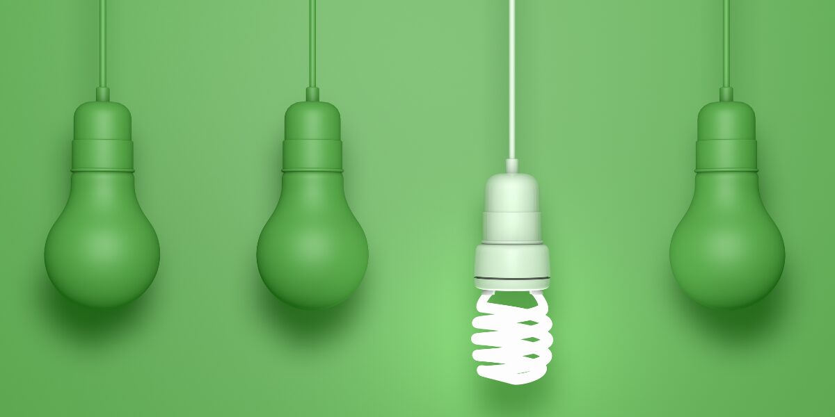 Four green light bulbs against a green background, with the third one standing out as a different, energy efficient spiral type.