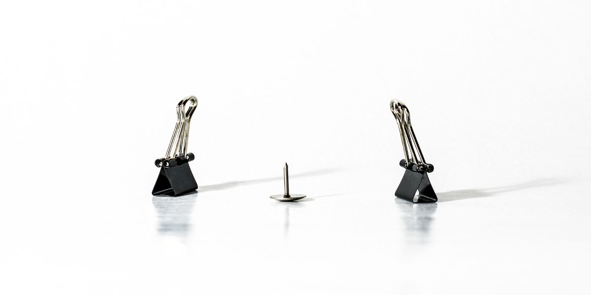 Two paper clips angled around a drawing pin representing a dispute.