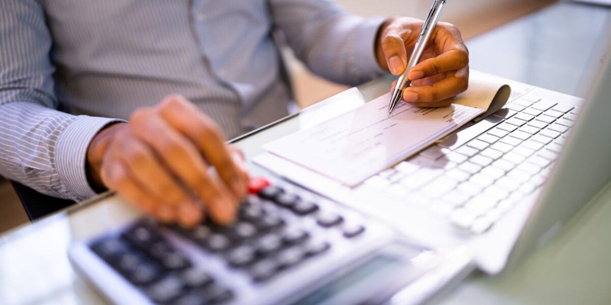 A man calculates tenant improvement compensation while writing notes on a piece of paper with a calculator beside him.