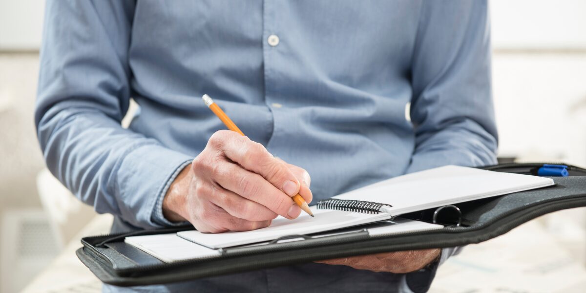 A man is focused on writing a notice of proposal for a care provider on a clipboard with a pen in hand.