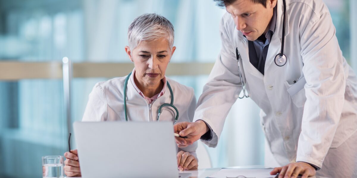 Two healthcare professionals discussing work pointing to a laptop